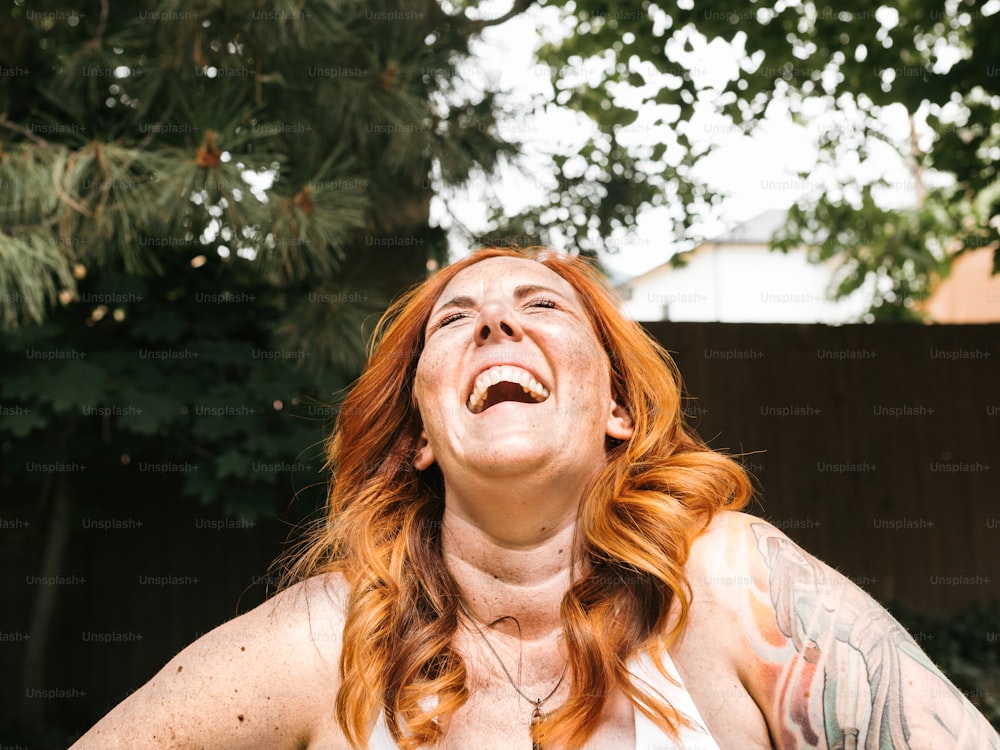 Eine Frau mit roten Haaren und Tätowierungen lacht
