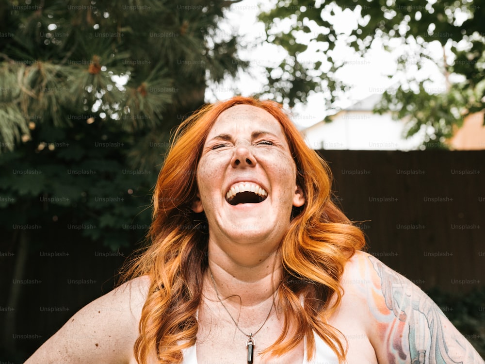Eine Frau mit roten Haaren und Tätowierungen lacht