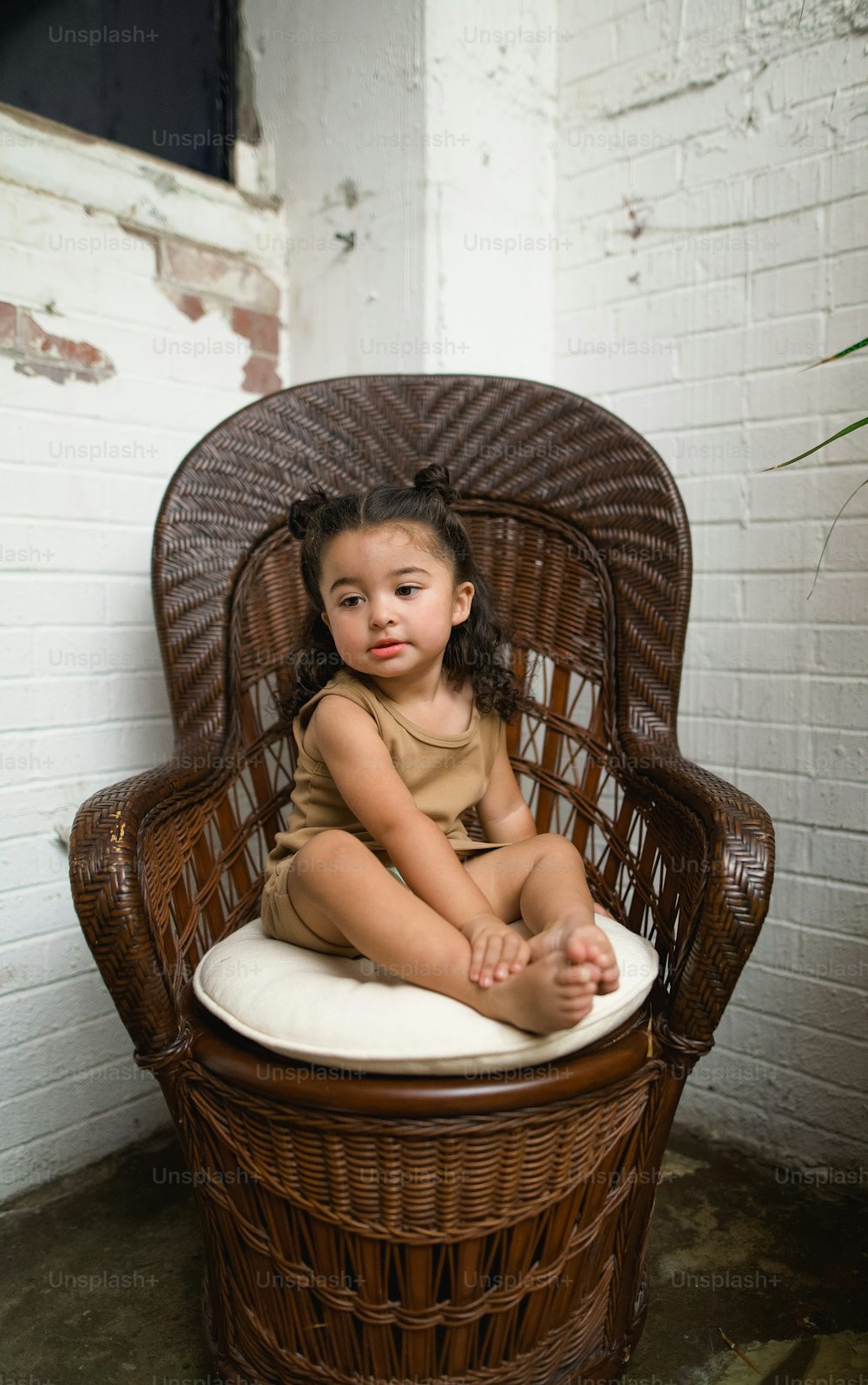 a little girl sitting on a wicker chair