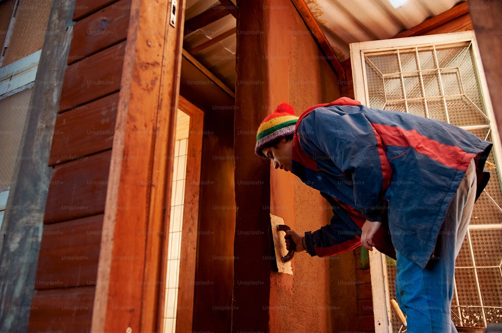 a man in a colorful hat and overalls working on a door