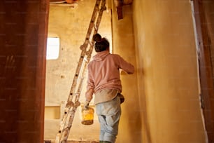 a woman climbing up a ladder to paint a wall