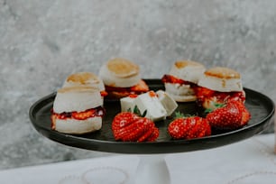 a black plate topped with mini sandwiches and strawberries