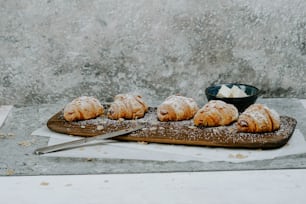 a wooden cutting board topped with pastries next to a bowl of cream