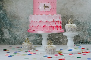 a pink and white cake on a table with cupcakes