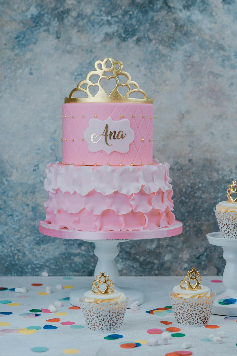 a pink and gold cake and cupcakes on a table