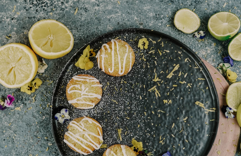 Un plato negro cubierto con galletas de limón junto a limones en rodajas