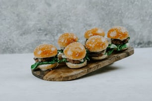 a group of mini hamburgers sitting on top of a wooden board