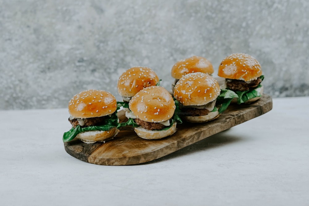 a group of mini hamburgers sitting on top of a wooden board