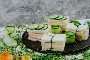 a black plate topped with cucumbers and slices of cake