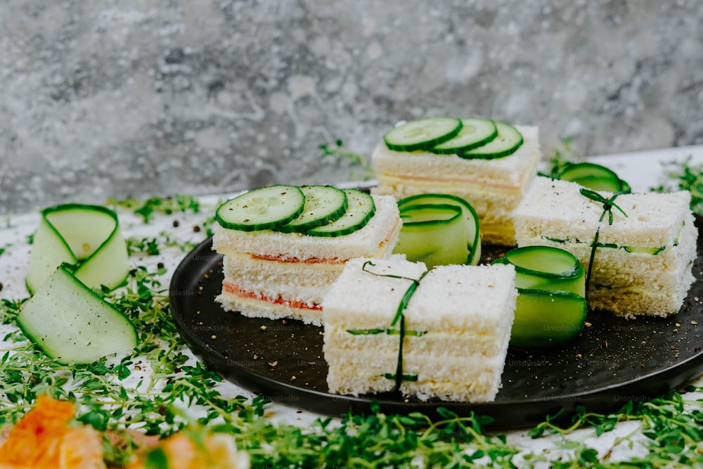 a black plate topped with cucumbers and slices of cake