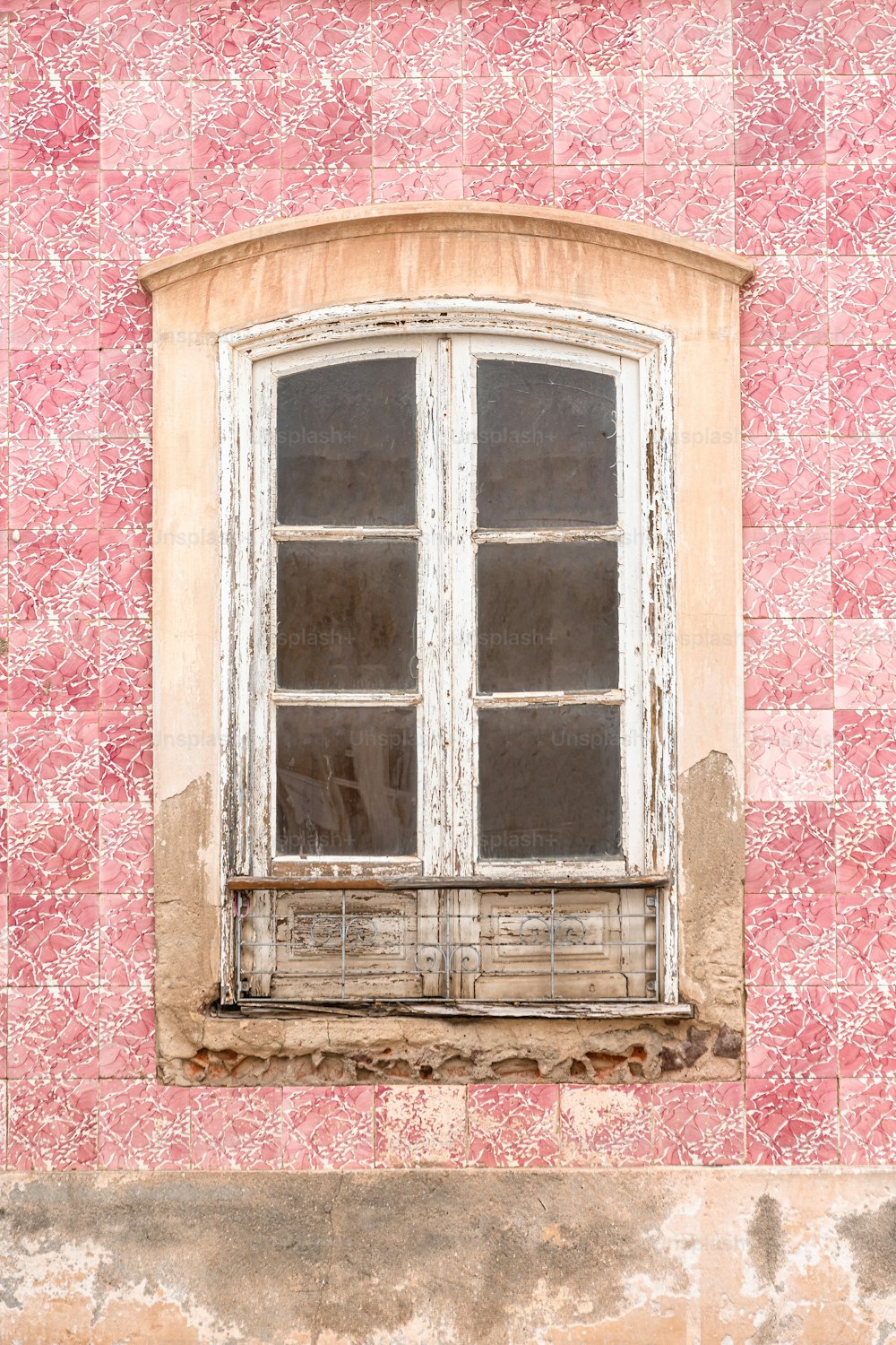 a window on a pink wall with a bench in front of it