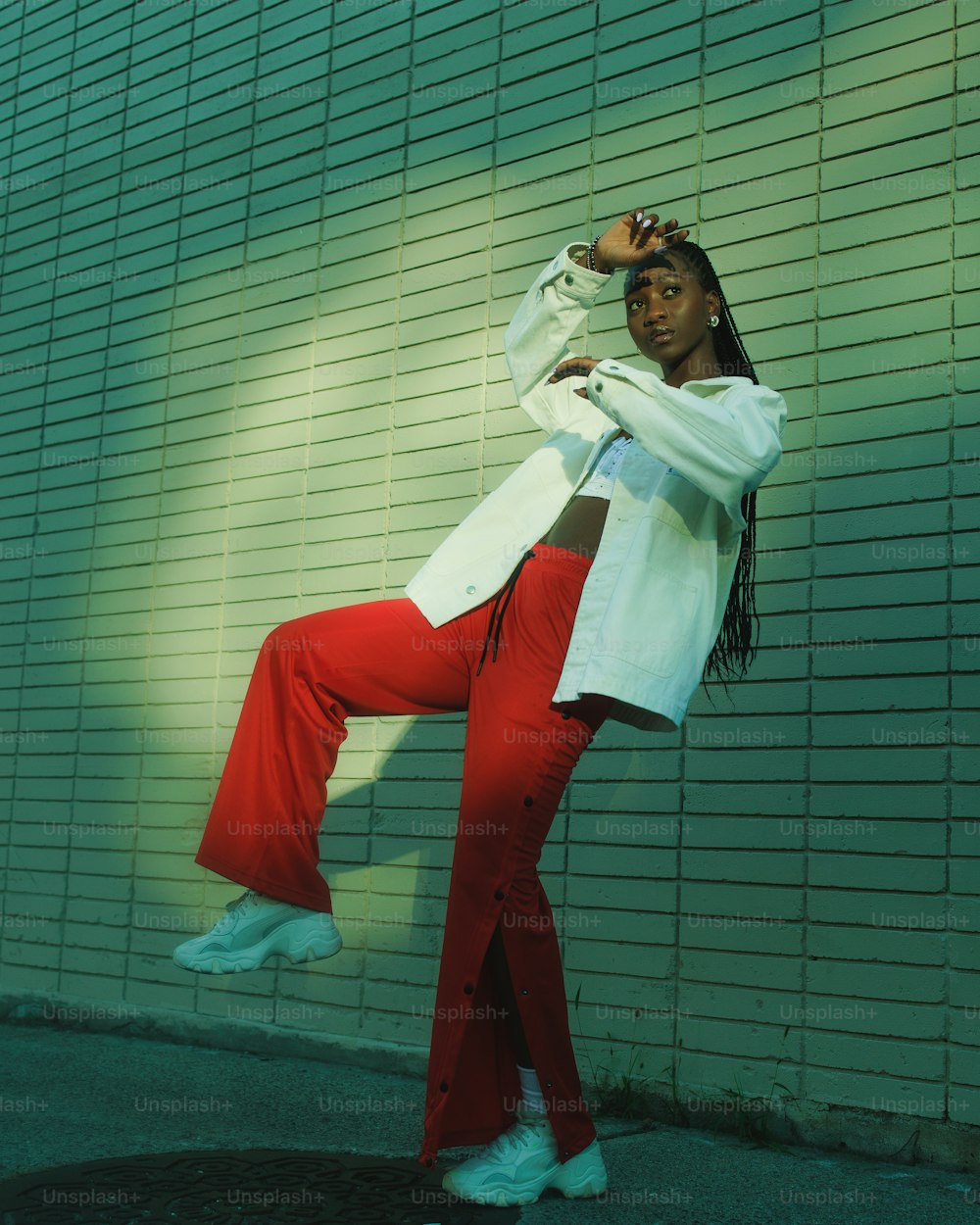 a woman in red pants and a white jacket leaning against a wall