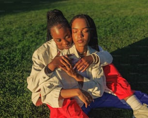 two women sitting on the grass looking at a cell phone