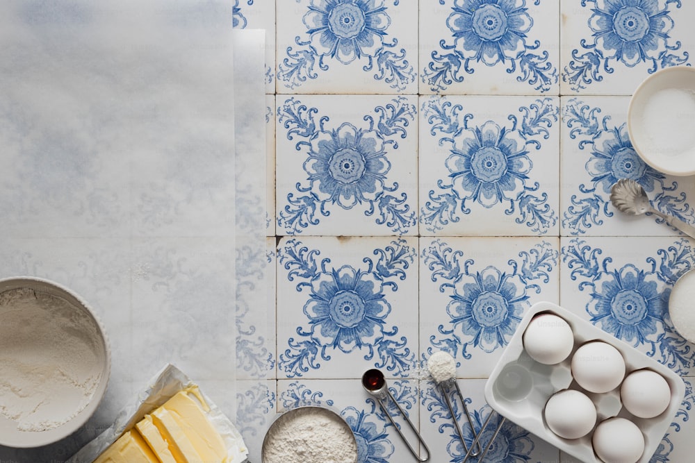 a blue and white tiled wall with bowls, spoons, and eggs