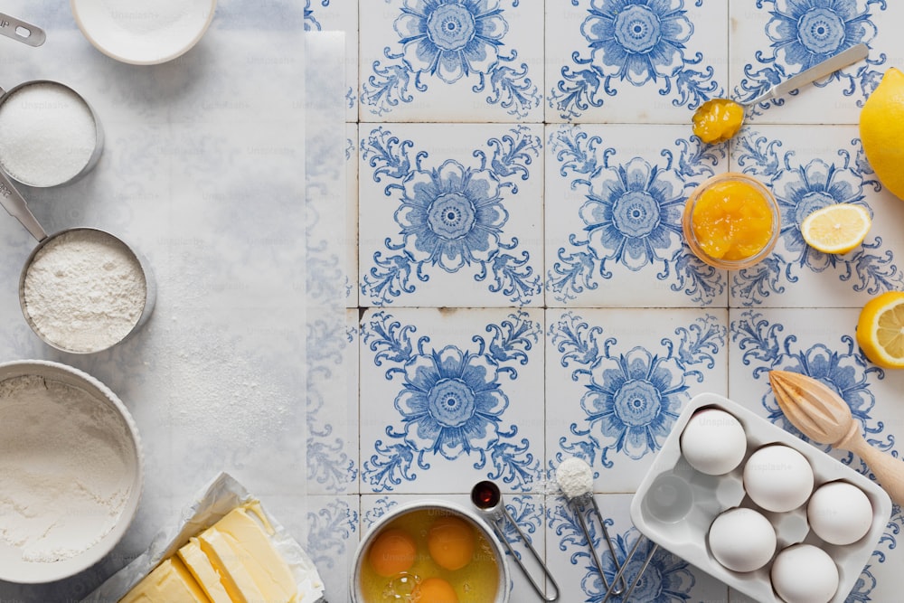 a blue and white tiled counter top with lemons, eggs, and other ingredients