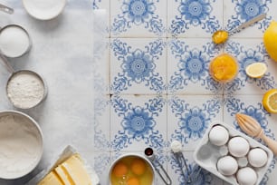 Un piano di lavoro piastrellato blu e bianco con limoni, uova e altri ingredienti