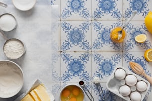 a blue and white tiled counter top with lemons, eggs, and other ingredients