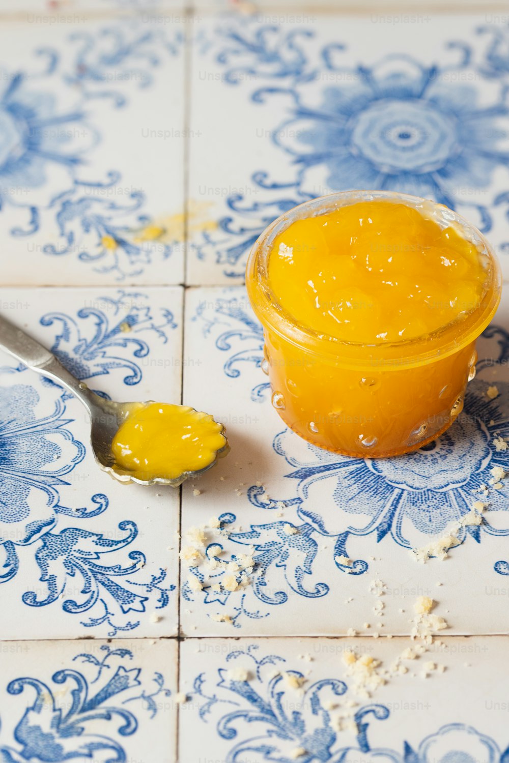 un cucchiaio con un barattolo di marmellata di arance su una piastrella blu e bianca