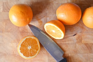 three oranges and a knife on a cutting board