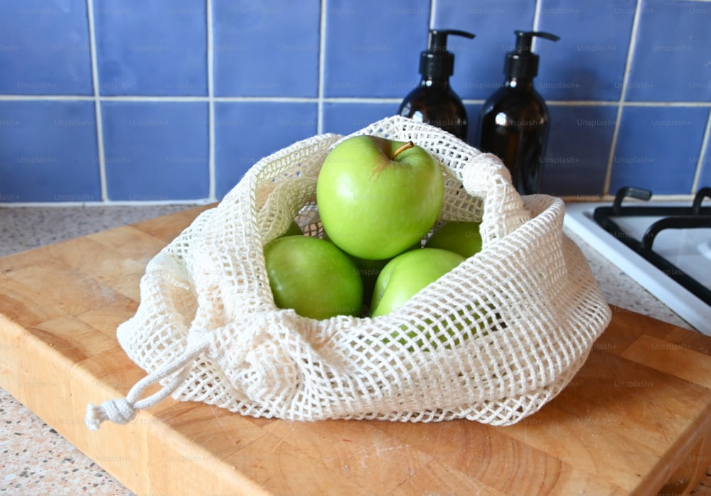 a bag of green apples sitting on top of a wooden cutting board