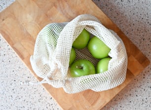 a bag filled with green apples sitting on top of a wooden cutting board