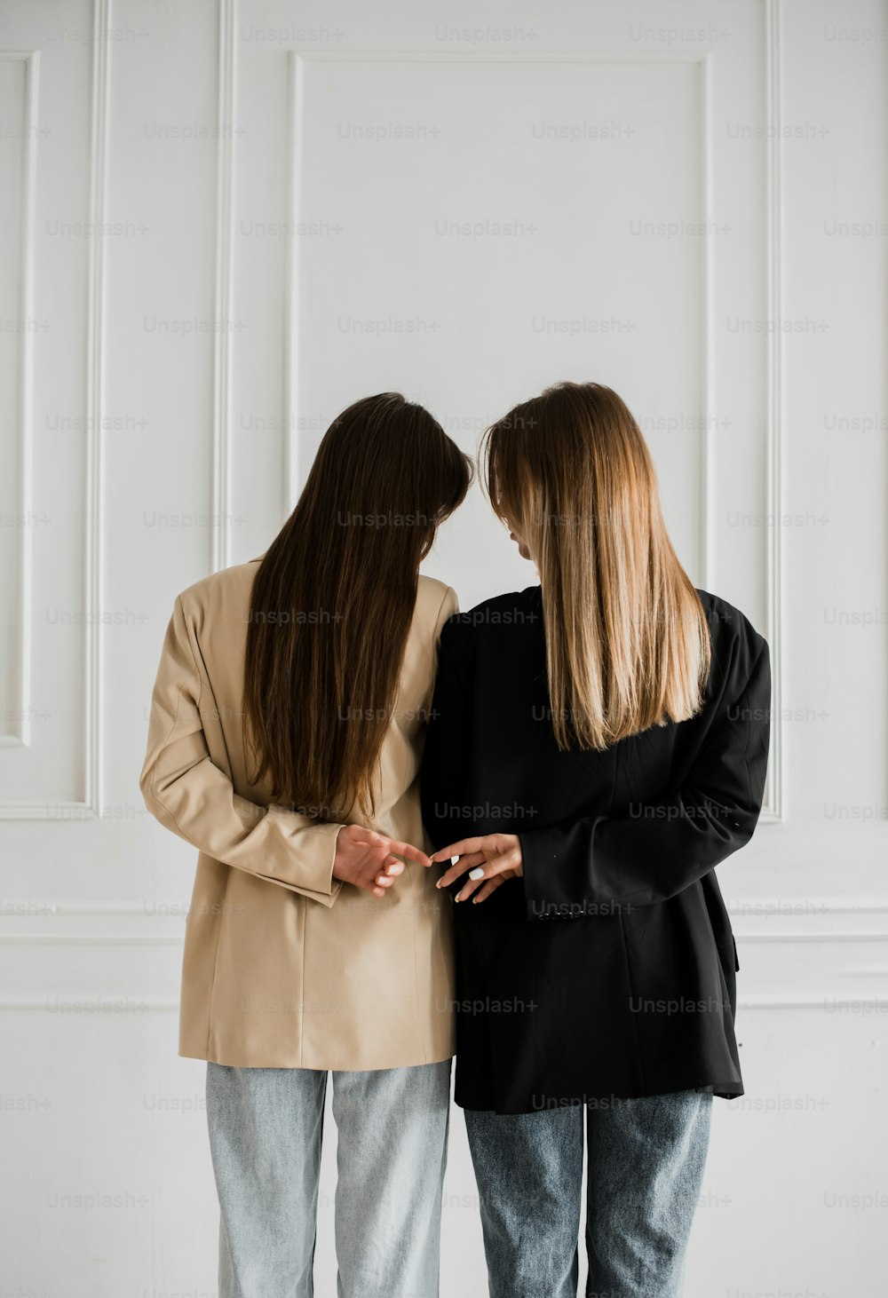 two women standing next to each other in front of a white wall