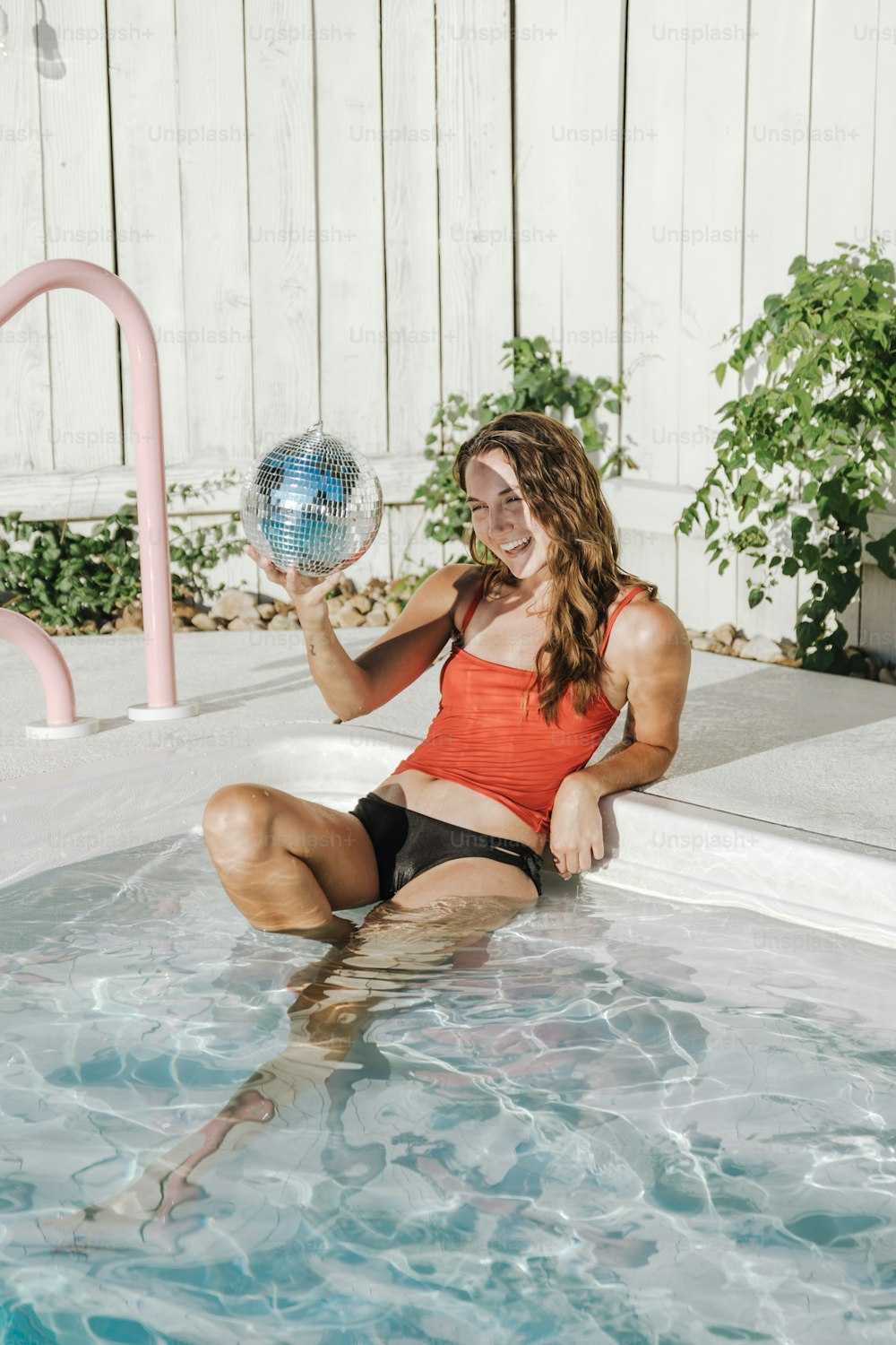 uma mulher sentada em uma piscina segurando uma bola de discoteca