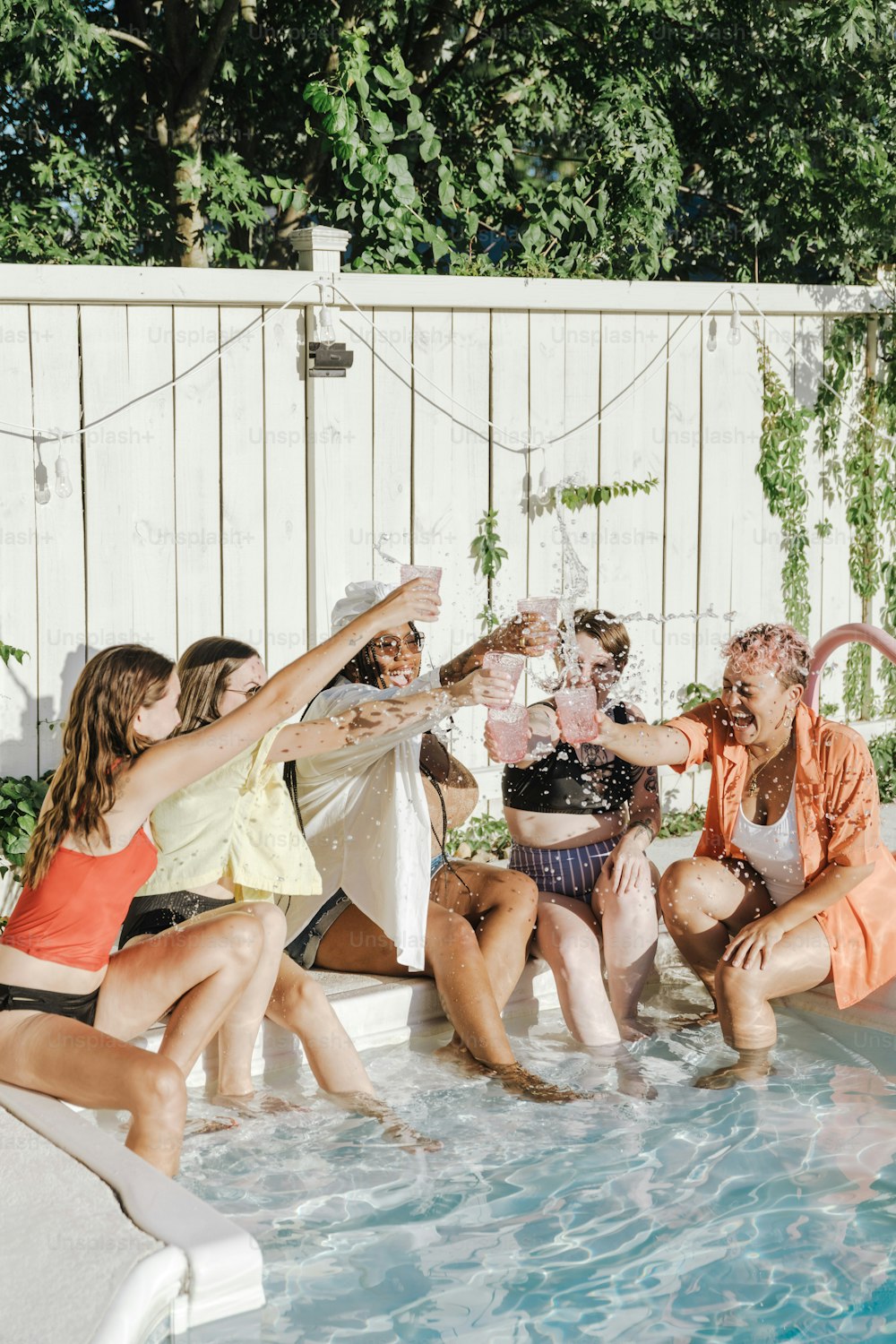 Un groupe de personnes assises autour d’une piscine buvant du champagne