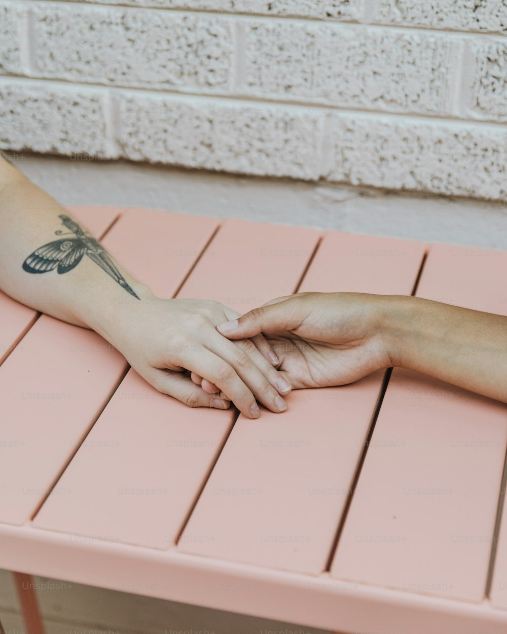 Eine Person mit einem Libellen-Tattoo auf dem Arm, die auf einer rosa Bank sitzt