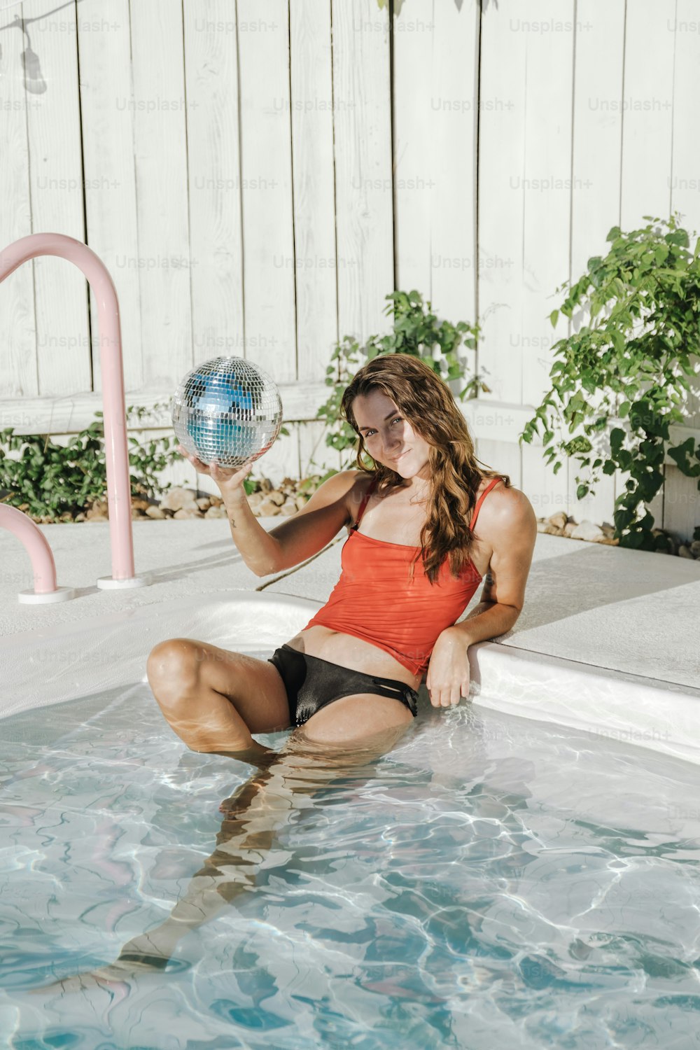a woman sitting in a pool holding a disco ball