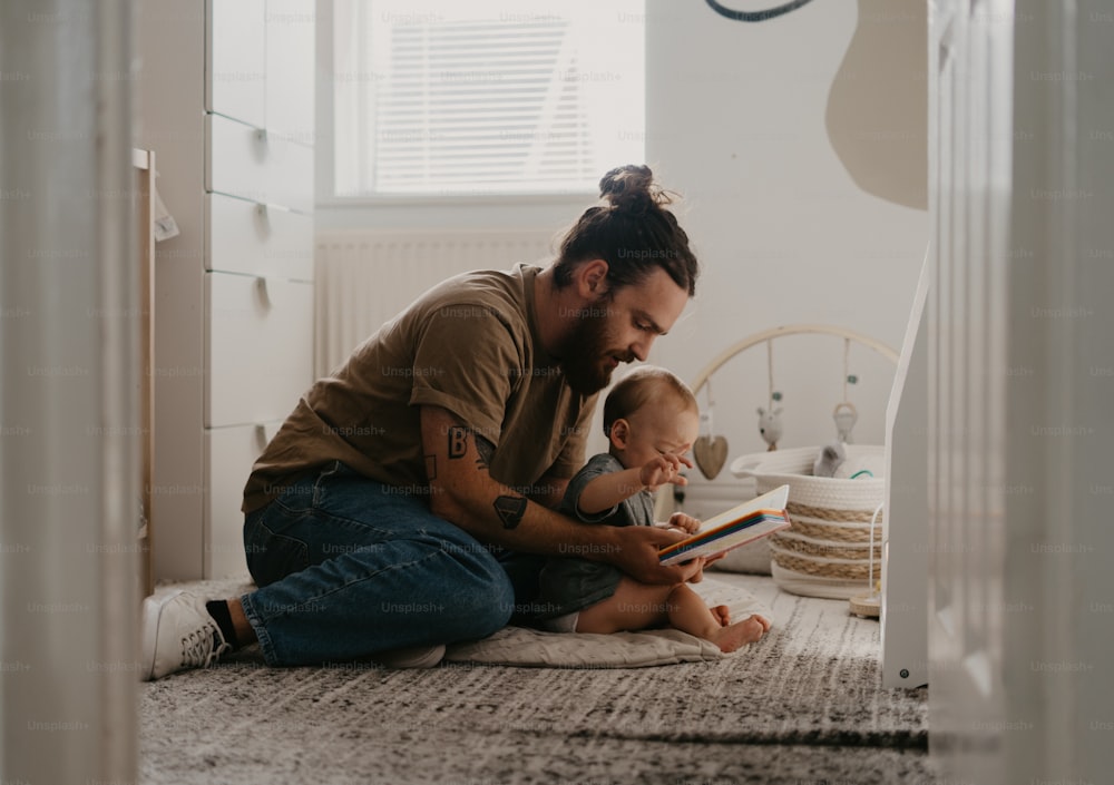 a man sitting on the floor reading a book to a baby