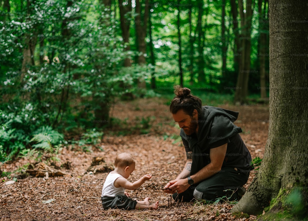 a man kneeling down next to a baby in the woods