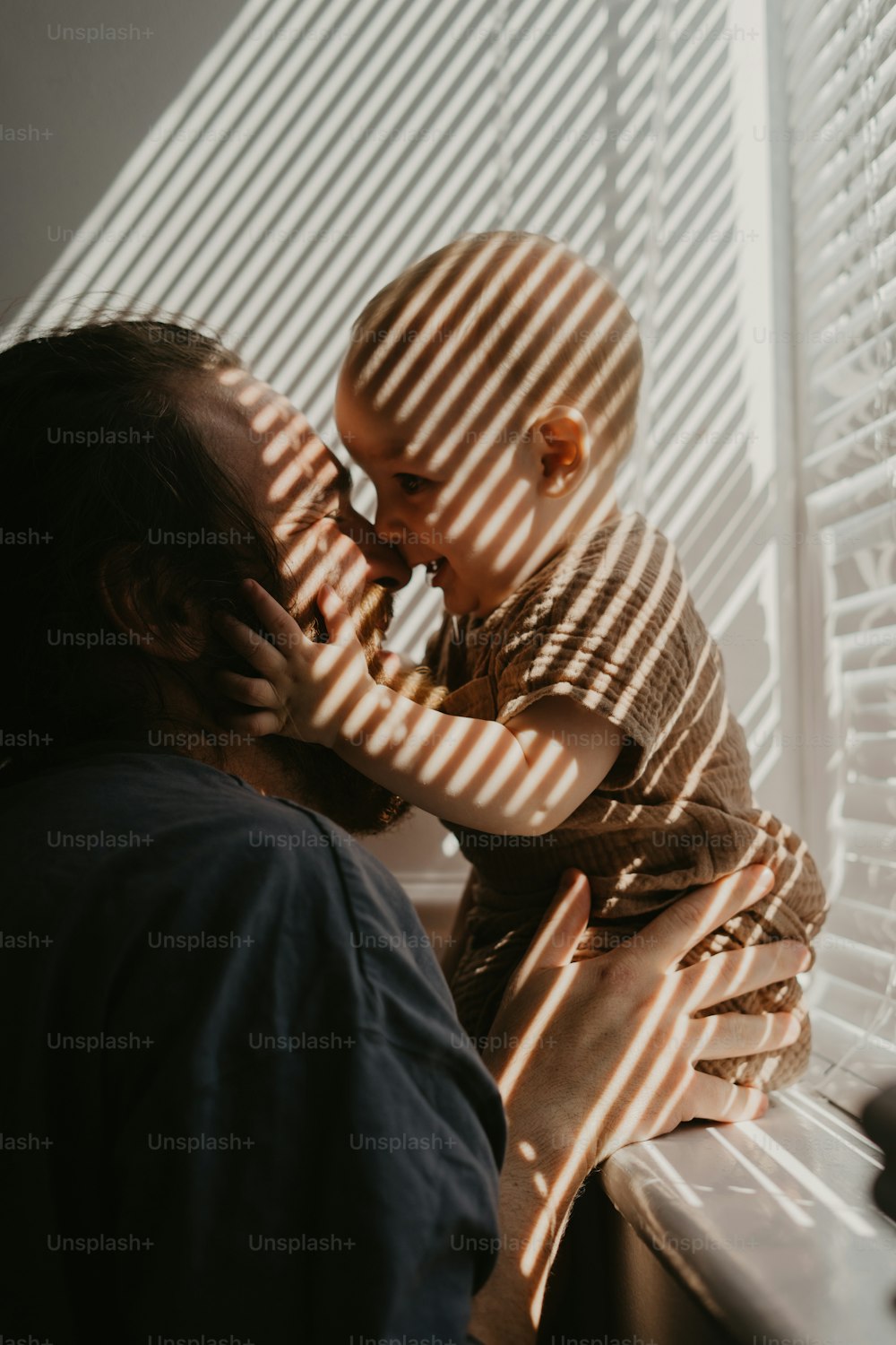 a man holding a baby next to a window