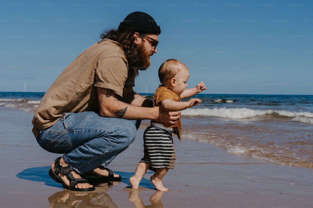 um homem ajoelhado ao lado de um bebê em uma praia
