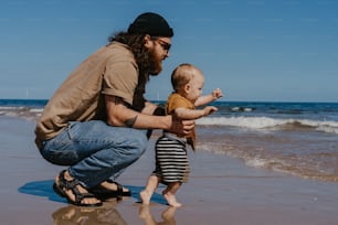 a man kneeling down next to a baby on a beach