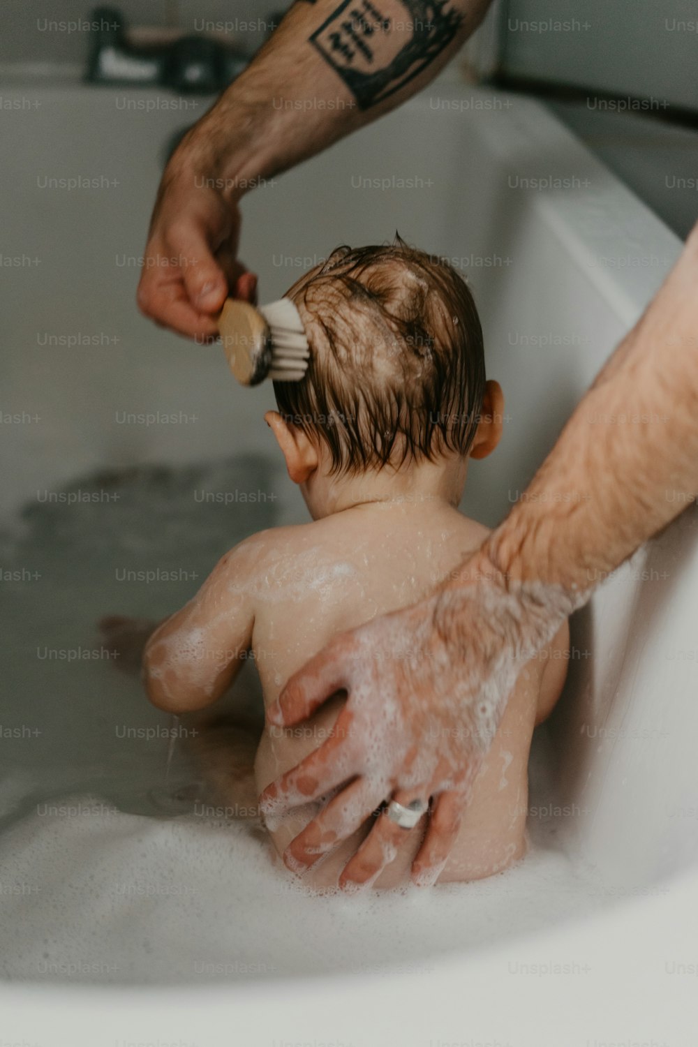 Un homme brossant les cheveux d’un enfant dans une baignoire