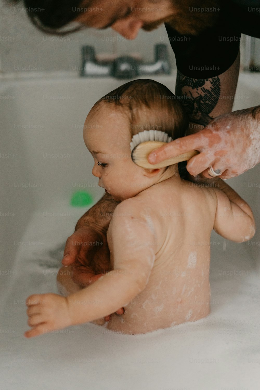 un bébé assis dans une baignoire en train d’être lavé avec une brosse