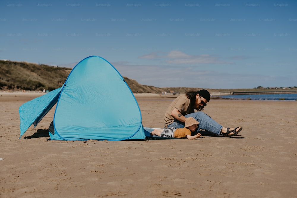 Ein Mann sitzt am Strand neben einem blauen Zelt