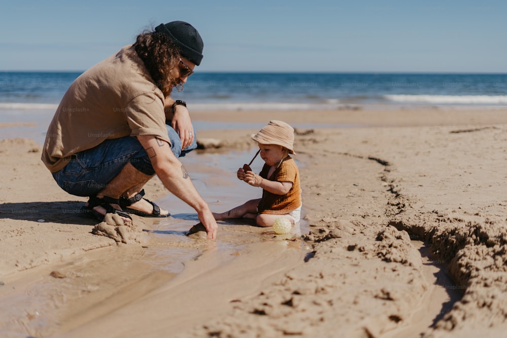 a man kneeling down next to a child on a beach
