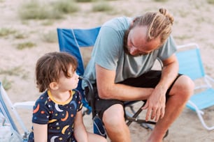 a man sitting next to a little boy on a beach