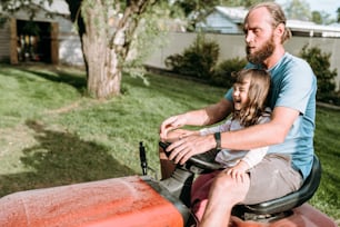 a man and a little girl riding on a lawn mower