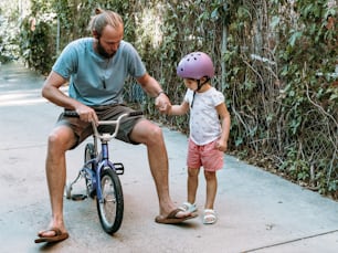a man sitting on a bike next to a little girl