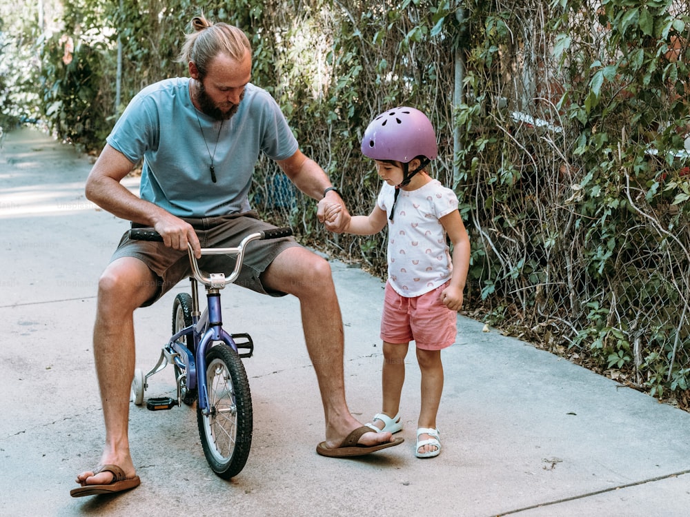 a man sitting on a bike next to a little girl