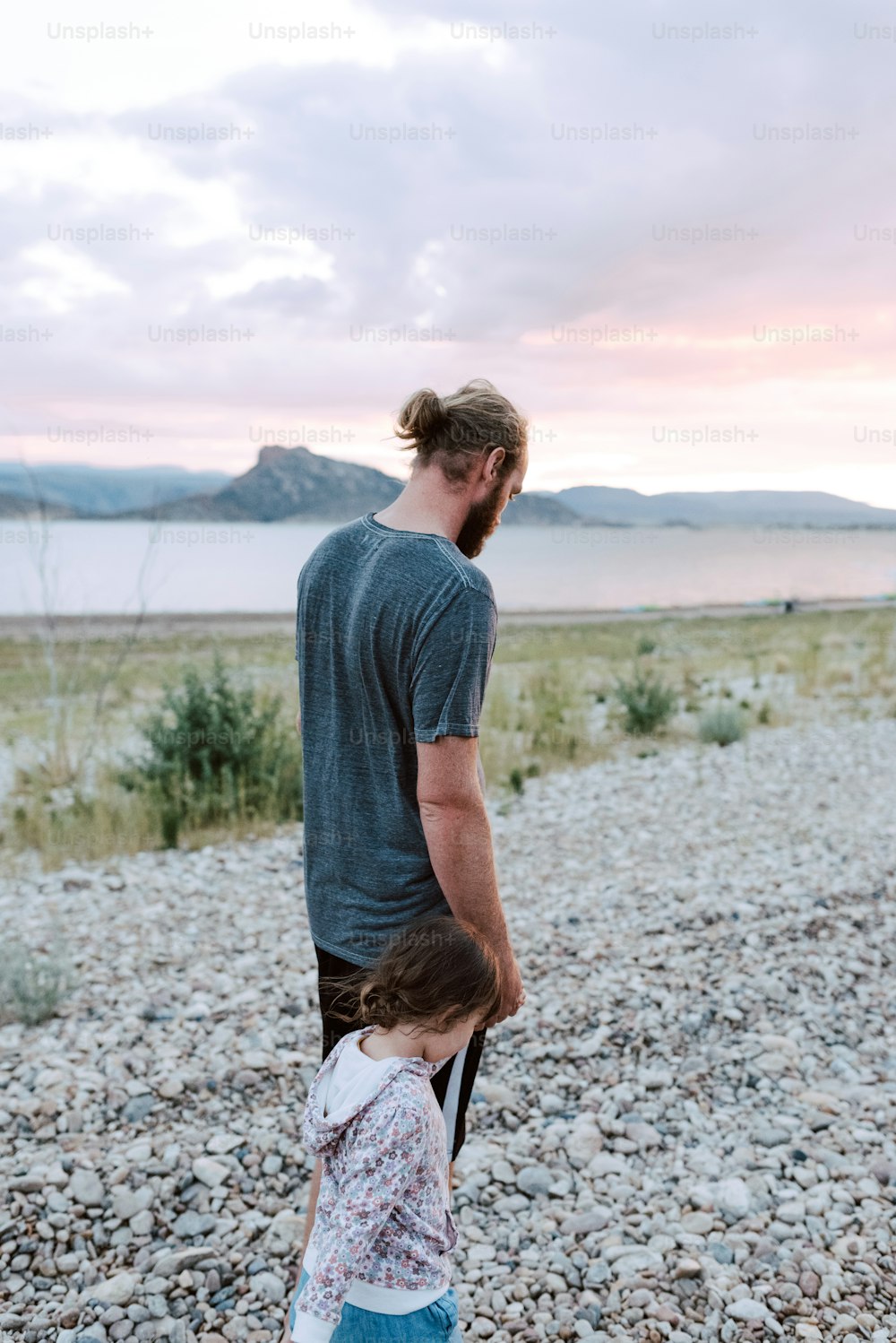 a man holding a little girl's hand on a rocky beach