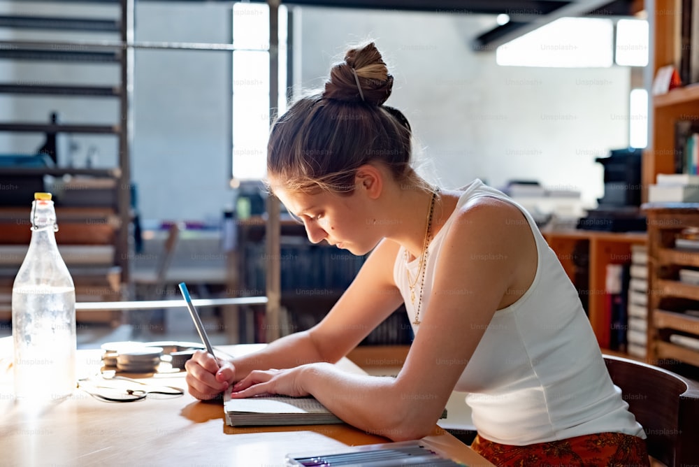 a woman sitting at a table writing on a book