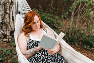 a woman sitting in a hammock reading a book