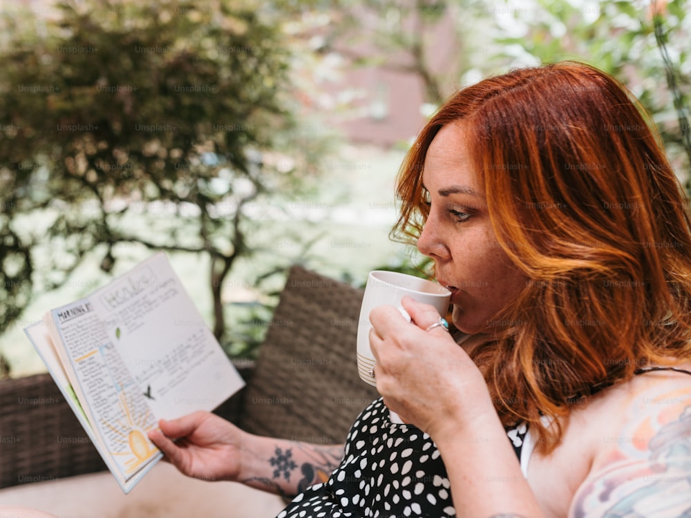 a woman drinking a cup of coffee and reading a book