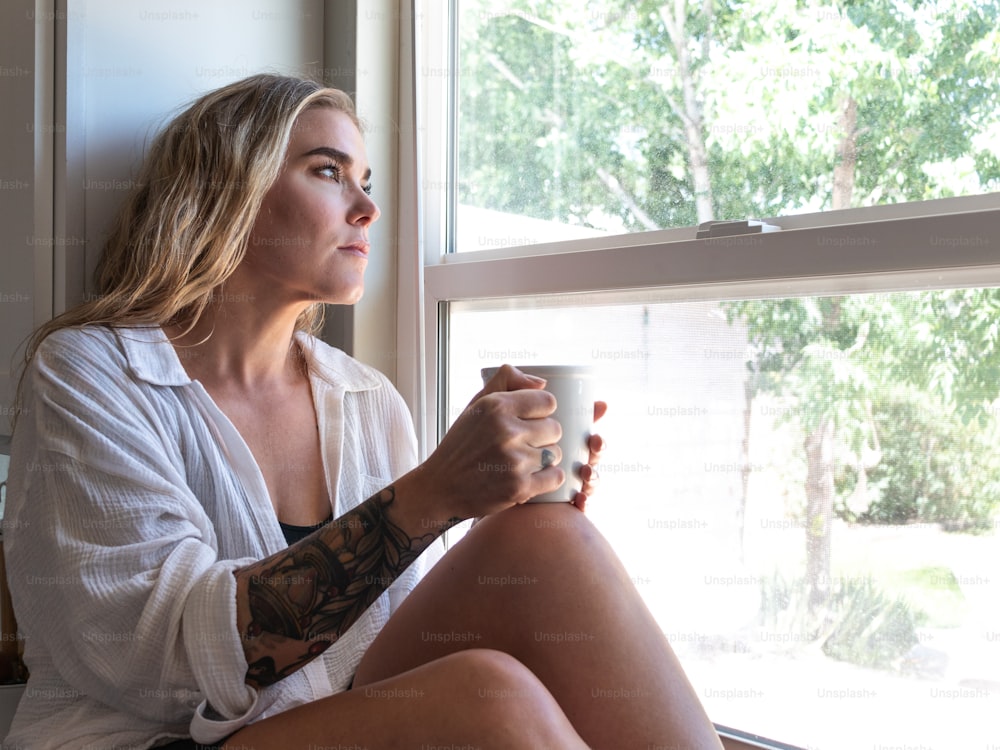 a woman sitting on a window sill holding a cup