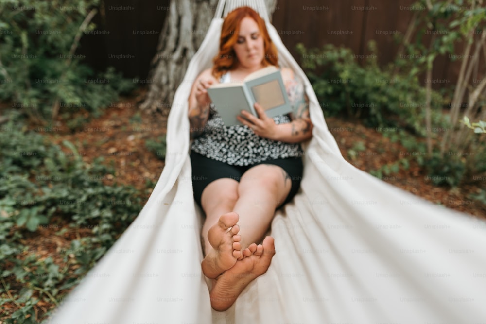 a woman sitting in a hammock reading a book