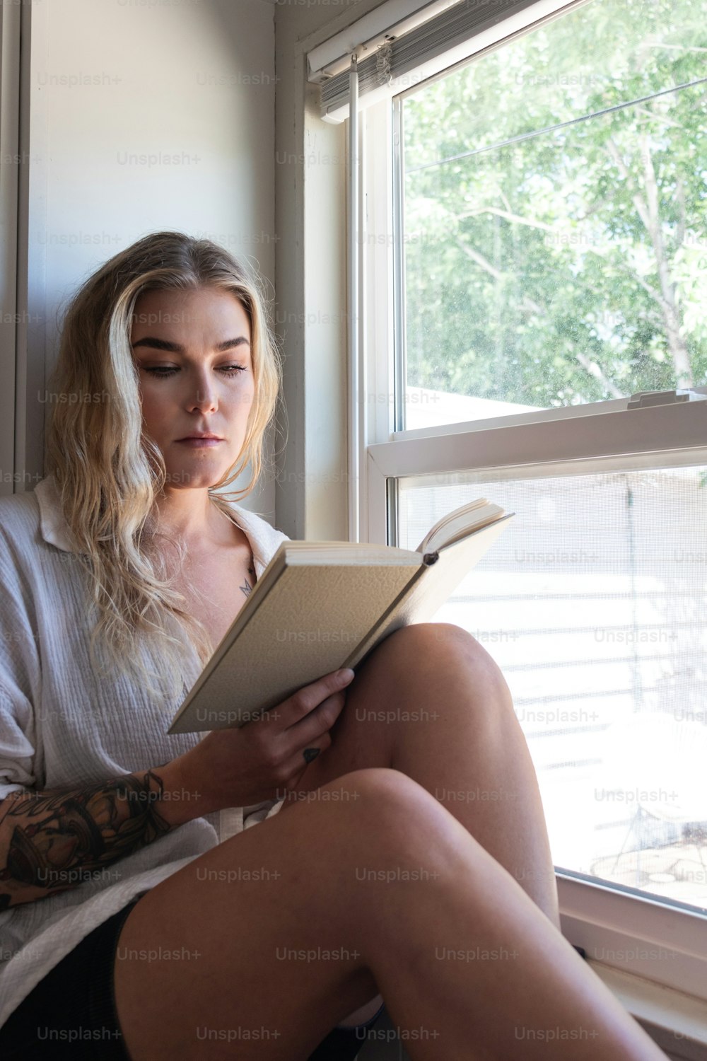 a woman sitting on a window sill reading a book